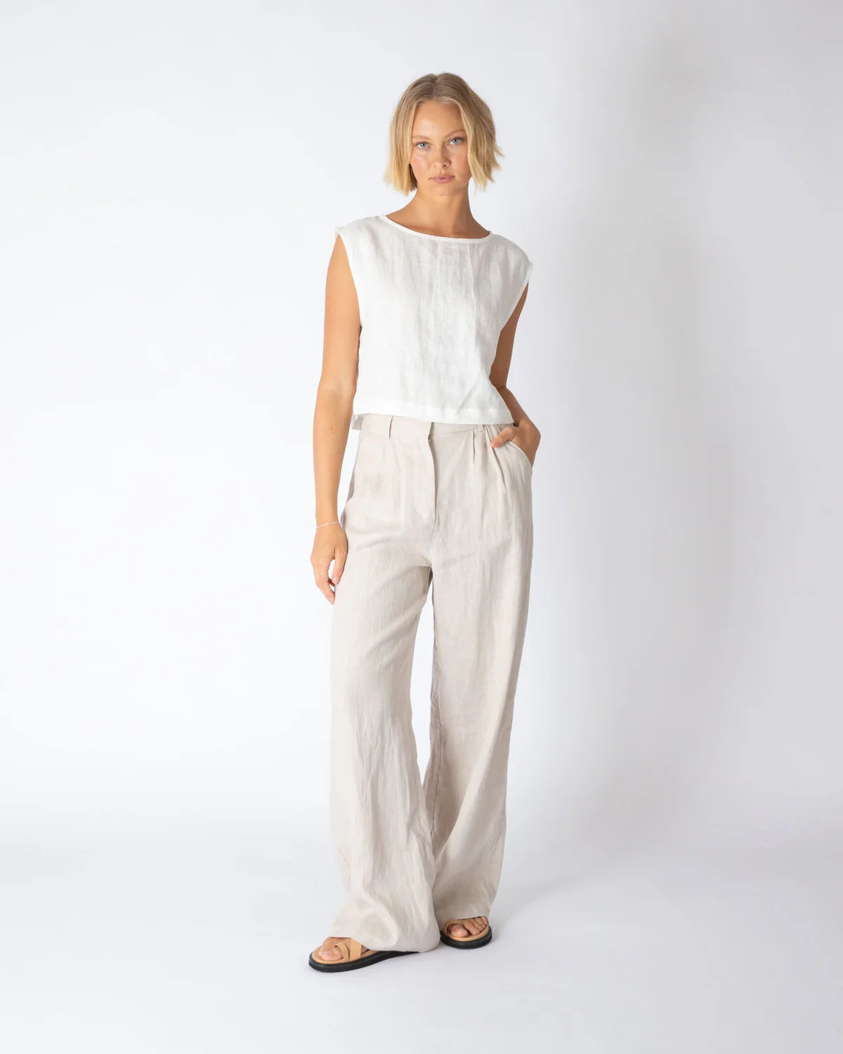 Woman wearing a white sleeveless top and beige pants on a white background