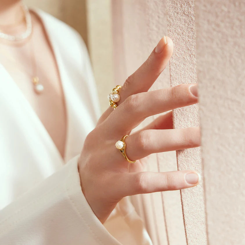 Hand wearing a gold ring with pearls against a soft background
