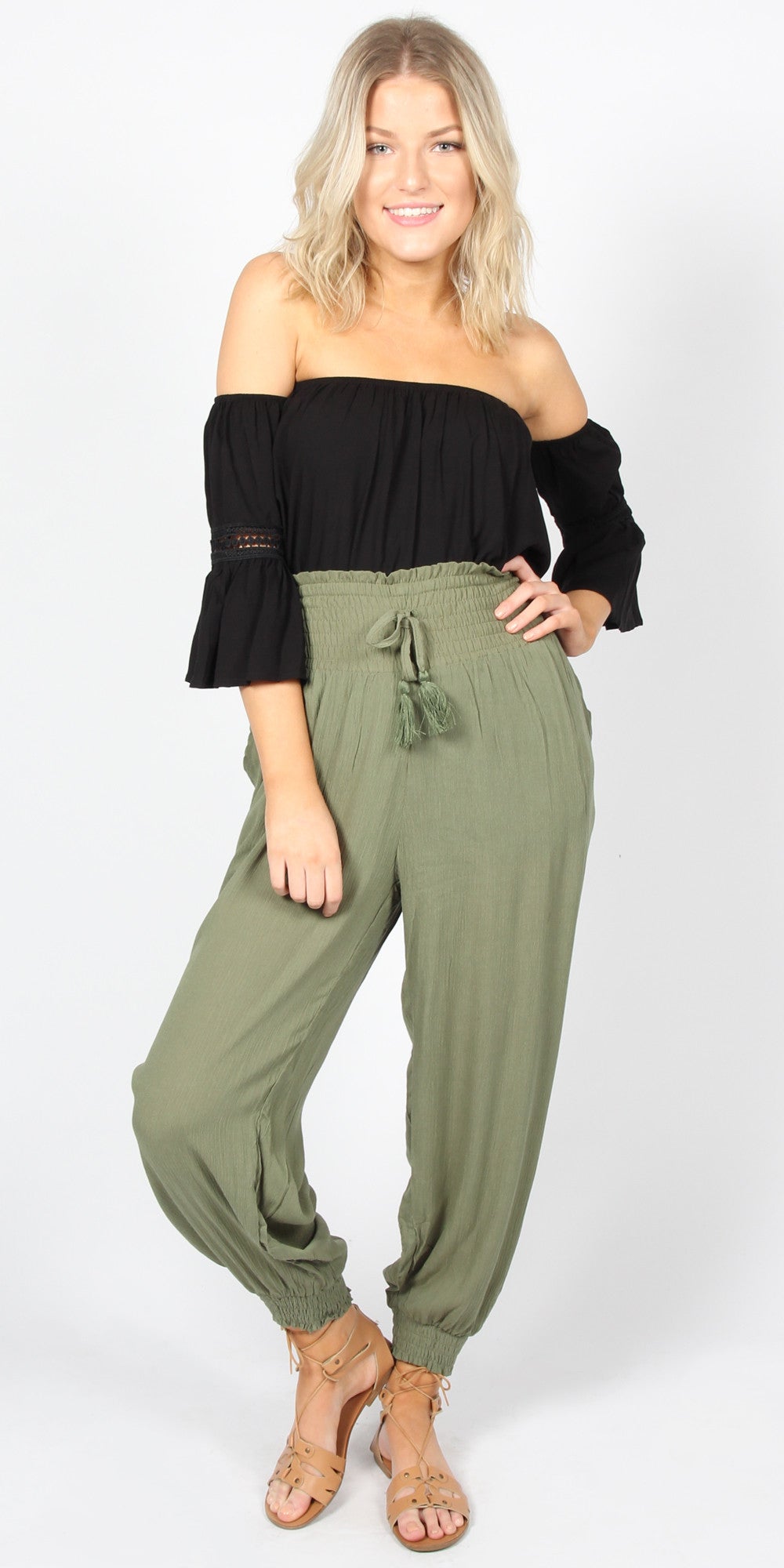 Woman wearing a black off-shoulder top and green jumpsuit on a white background